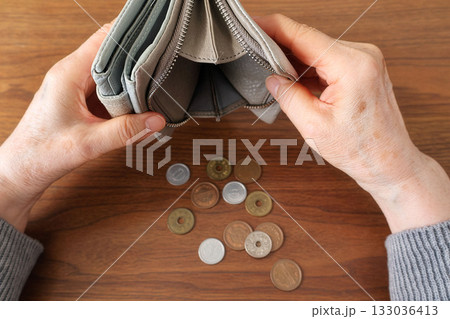 財布をひっくり返すシニア女性の手と机上の小銭 財布をひっくり返すシニア女性の手と机上の小銭 133036413