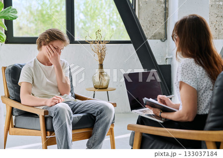 Sad teenage boy in mental therapy session, talking with behavioral psychologist Sad teenage boy in mental therapy session, talking with behavioral psychologist 133037184