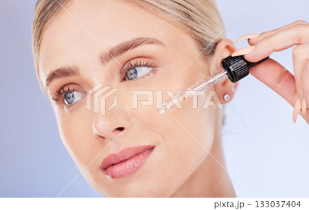 Face, beauty and skincare of woman with serum in studio isolated on a blue background. Dermatology cosmetics, thinking closeup and female model apply hyaluronic acid, retinol or essential oil product 133037404