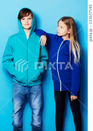 Fashion, portrait and teenager models in a studio with a casual, cool and stylish outfit. Youth, friendship and young boy and girl posing together with trendy apparel style by a blue background. Fashion, portrait and teenager models in a studio with a casual, cool and stylish outfit. Youth, friendship and young boy and girl posing together with trendy apparel style by a blue background. 133037595
