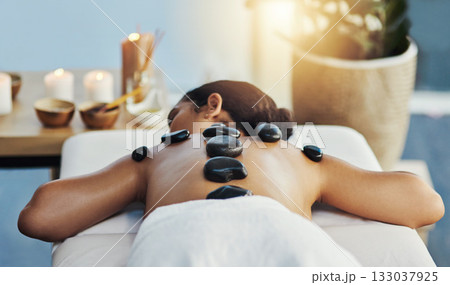 Woman, relax and rock in back massage at spa for skincare, beauty or body treatment on bed at resort. Calm female lying in relaxation with hot rocks or stone pile in therapy, zen or wellness at salon 133037925