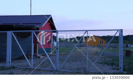 Red farmhouse behind white metal gates and orange building in the distance, farm provincial landscape with residential and outbuildings, no people, farmer's housing in the countryside Red farmhouse behind white metal gates and orange building in the distance, farm provincial landscape with residential and outbuildings, no people, farmer's housing in the countryside 133039000