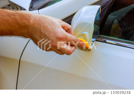 Car applying protective film to side mirror of vehicle  to safeguard against scratches damage 133039238