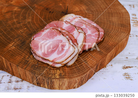 Slices of cured meat displayed on rustic wooden cutting board in home kitchen setting Slices of cured meat displayed on rustic wooden cutting board in home kitchen setting 133039250