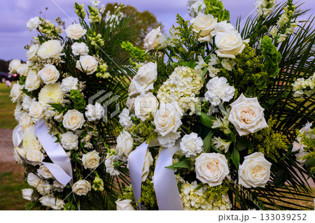 Floral arrangements featuring white roses, green foliage at memorial site during tranquil afternoon Floral arrangements featuring white roses, green foliage at memorial site during tranquil afternoon 133039252