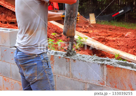 Construction worker pouring concrete into masonry block wall during home project Construction worker pouring concrete into masonry block wall during home project 133039255