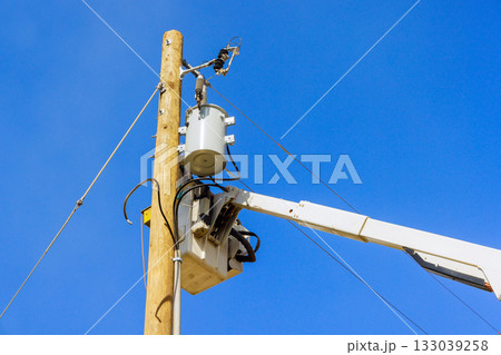 Workers performing maintenance on an electrical transformer atop utility pole under clear blue skies Workers performing maintenance on an electrical transformer atop utility pole under clear blue skies 133039258