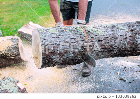 Person cutting wood with a chainsaw on a sunny day in an outdoor setting 133039262