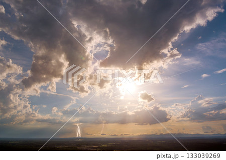 Dramatic thunderstorm with lightning over green landscape during sunset in rural area 133039269