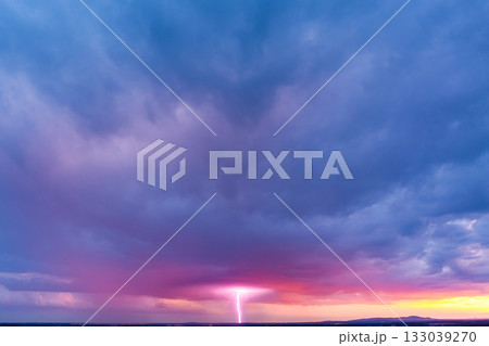 Colorful sunset sky with dramatic lightning striking over horizon during stormy evening 133039270