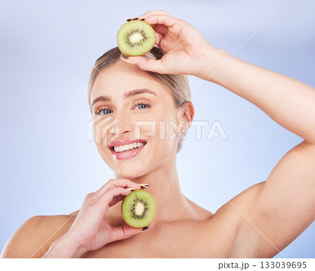 Portrait, kiwi and woman with skincare, cosmetics and smile with girl against a blue studio background. Face, female and lady with fruit, morning routine or grooming for smooth, clear or natural care Portrait, kiwi and woman with skincare, cosmetics and smile with girl against a blue studio background. Face, female and lady with fruit, morning routine or grooming for smooth, clear or natural care 133039695