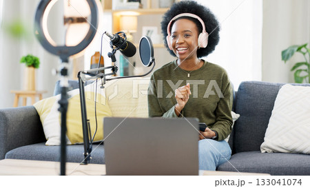 Headphones, laptop and black woman on microphone in podcast at home in living room of influencer. Technology, smile and content creator on mic for broadcast, communication and radio talk show on sofa 133041074