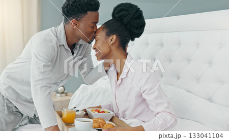 Breakfast in bed, love and black couple kissing on their honeymoon, birthday or anniversary in a hotel room. Happy man and woman bonding in a bedroom for love while on vacation or holiday together 133041104
