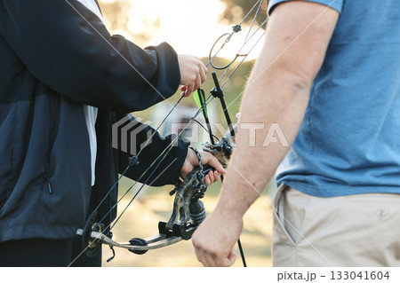 Shooting range, bow and archery sports training with a woman and man outdoor for target practice. Hands of archer and athlete person for competition game or learning to aim, exercise and shoot arrow 133041604