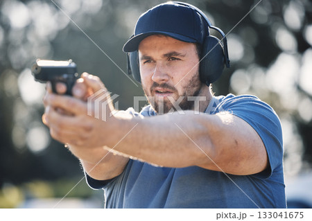Man, gun and learning to aim at shooting range outdoor for security target training. Face of person train with safety gear headphones for focus on sport competition with firearm weapon in hands Man, gun and learning to aim at shooting range outdoor for security target training. Face of person train with safety gear headphones for focus on sport competition with firearm weapon in hands 133041675