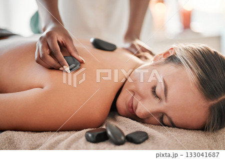 Woman, hot stone massage and masseuse, hand and zen with holistic therapy and spa treatment for back. Calm, peace of mind and face, healing and stress relief with self care at wellness resort Woman, hot stone massage and masseuse, hand and zen with holistic therapy and spa treatment for back. Calm, peace of mind and face, healing and stress relief with self care at wellness resort 133041687
