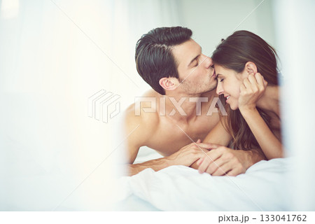 Romantic, love and man kissing his wife in the morning after an anniversary, date or intimate time in bed. Gratitude, relax and young couple in the bedroom showing care and bonding for valentines day 133041762