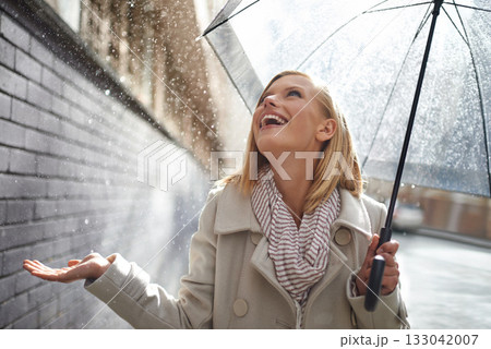 Smile, excited woman and rain in the city with umbrella, freedom and happiness on holiday. Winter weather, raining or urban street with a young female person on a sidewalk and travel vacation outdoor 133042007