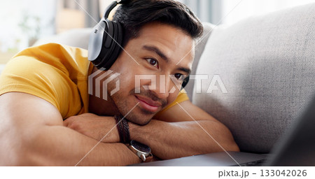 Smile, headphones and laptop with man on sofa for streaming service, film website and comfortable. Movie subscription, watching series and entertainment with person in living room of home for search 133042026