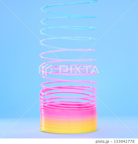 Rainbow slinky toy, spring and plastic product in studio isolated against a blue background mockup. Flexible toys, colorful spirals and childhood item stretched out for playing, having fun and games. 133042778