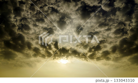 Cumulus sunset clouds with sun setting down 133043310