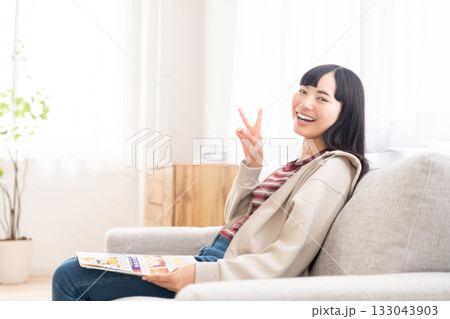 ソファーに座って雑誌を読んでいる若い女性 ソファーに座って雑誌を読んでいる若い女性 133043903