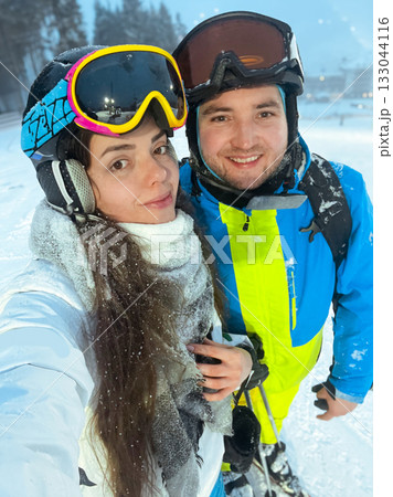 Couple enjoying a winter day on the ski slopes in a snowy mountain landscape with ski gear and equipment amidst beautiful scenery 133044116