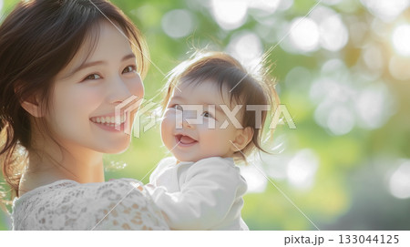 公園の新緑を背景に笑顔の赤ちゃんと若い母親 公園の新緑を背景に笑顔の赤ちゃんと若い母親 133044125