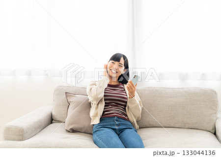 ソファーに座ってスマホで音楽を聴いている若い女性 ソファーに座ってスマホで音楽を聴いている若い女性 133044136