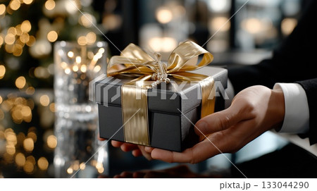 Person holding elegant gift box with golden ribbon, offering a thoughtful present for celebratory occasions and special moments like holidays, anniversaries, or Christmas 133044290