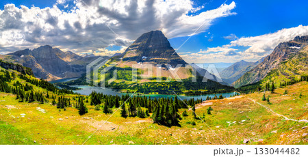 A wide panoramic view of Hidden Lake and Bearhat Mountain from the Logan Pass overlook in Glacier National Park, Montana. A green meadow is in the foreground under a dramatic cloudy sky 133044482