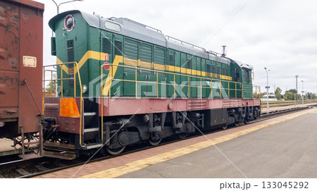 Powerful diesel locomotive pulls a heavy freight car. Freight train on the tracks, seen from behind. Summer clouds loom 133045292
