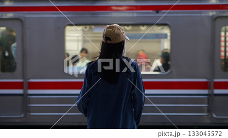 Blurred image of a woman standing on a train platform watching a train pass by. 133045572
