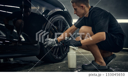 Detailer spraying cleaning solution on car wheel during detailing service 133045650