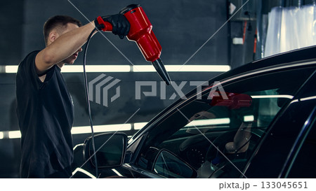 Worker using red air blower to dry car windshield after detailing wash 133045651