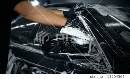 Hands washing car mirror with foam sponge during auto detailing Hands washing car mirror with foam sponge during auto detailing 133045654