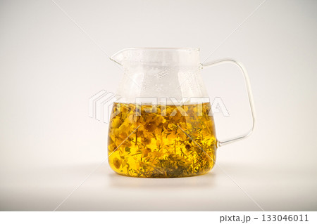 A glass of Chamomile tea with flowers floating in it. The tea is yellow and the flowers are white A glass of Chamomile tea with flowers floating in it. The tea is yellow and the flowers are white 133046011