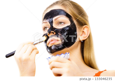 Woman applying black mud mask to face Woman applying black mud mask to face 133046235