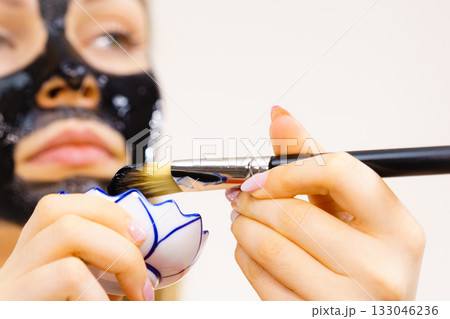 Woman applying black mud mask to face 133046236