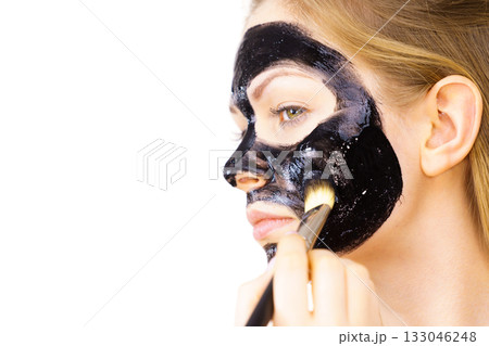 Woman applying black mud mask to face 133046248