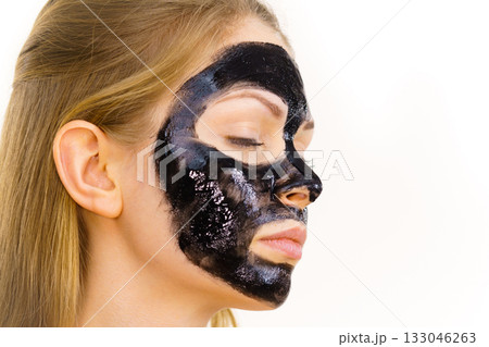 Woman applying black cleanser mask to face 133046263