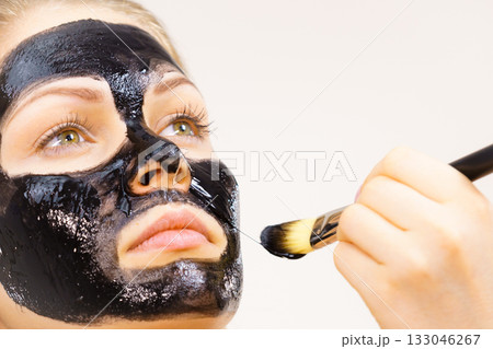 Woman applying black mud mask to face Woman applying black mud mask to face 133046267