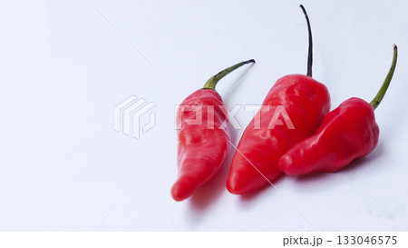 A bunch of bright red chilies with green stems arranged on a white background 133046575