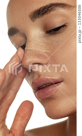 Side view of woman with nasal bandage gently touching face during recovery 133046886