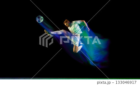 Soccer player performing midair kick surrounded by glowing blue and green light motion Soccer player performing midair kick surrounded by glowing blue and green light motion 133046917