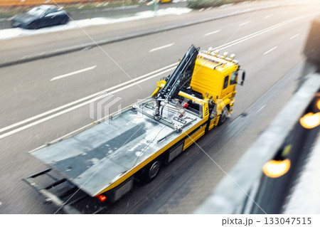 Yellow empty tow truck drives fast rush on wet winter road at city on cold snowy day. Motion blur and perspective create a dynamic scene of transport and urban activity. Support and assistance Yellow empty tow truck drives fast rush on wet winter road at city on cold snowy day. Motion blur and perspective create a dynamic scene of transport and urban activity. Support and assistance 133047515