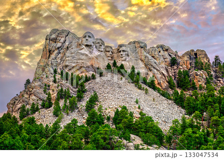 Mount Rushmore National Memorial in South Dakota. The granite carving of four presidents is lit under a dramatic, colorful cloudy sky at sunset 133047534