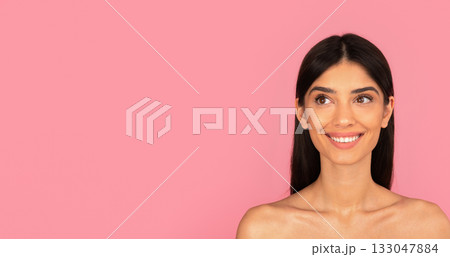 Smiling young woman with bare shoulders looking aside on pink background Smiling young woman with bare shoulders looking aside on pink background 133047884