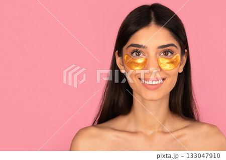 Smiling young woman wearing gold under-eye patches for skincare and rejuvenation 133047910