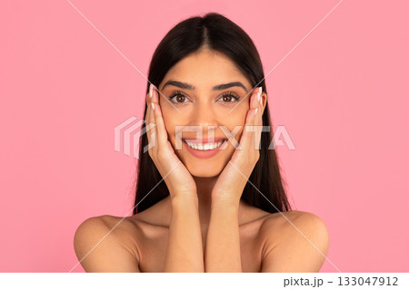Happy young woman smiling with hands on cheeks against pink background 133047912